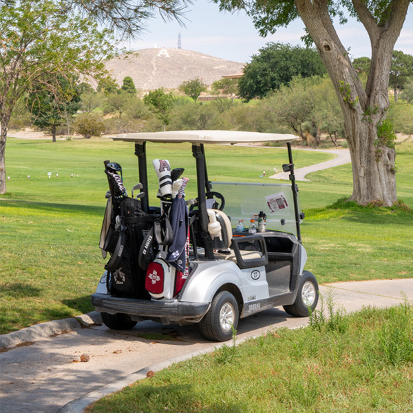Golf cart parked on a pathway at a golf course with clubs in the back.