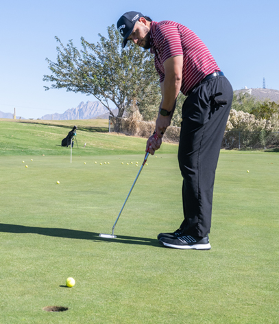 Golfer focusing on putting on the green with a distant view of mountains in the background.